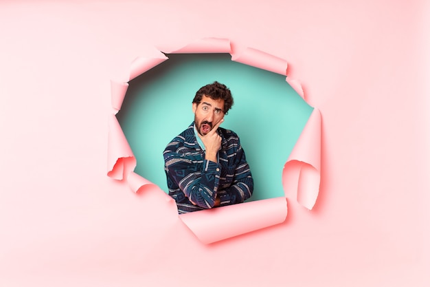 Young crazy bearded man. shocked or surprised expression. paper hole empty background concept