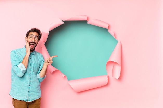 Young crazy bearded man shocked or surprised expression paper hole empty background concept