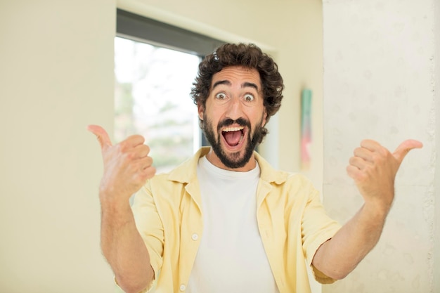 Фото Молодой сумасшедший бородатый мужчина радостно улыбается и выглядит счастливым, чувствует себя беззаботным и позитивным, подняв оба больших пальца вверх
