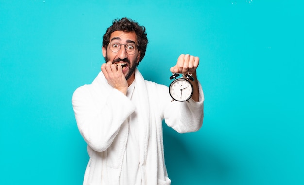 Young crazy bearded man wearing bathrobe and an alarm clock