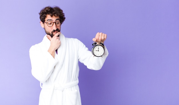 Young crazy bearded man  wearing bathrobe holding an alarm clock