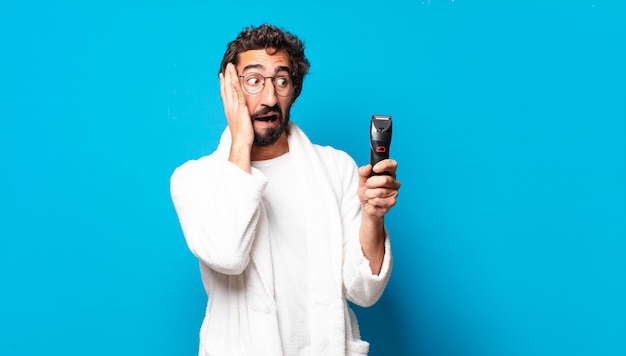 Young crazy bearded man wearing bathrobe shaving concep