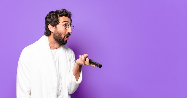 Young crazy bearded man wearing bathrobe with a television remote control