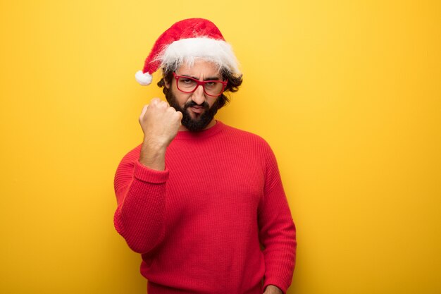 Young crazy bearded man wearing red glasses and santa claus hat 