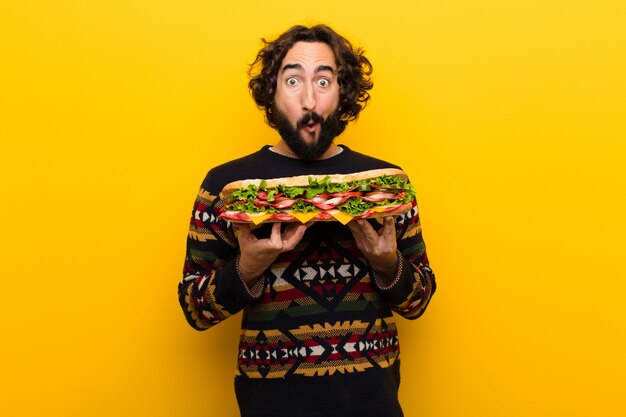 Giovane pazzo uomo barbuto con un panino gigante.