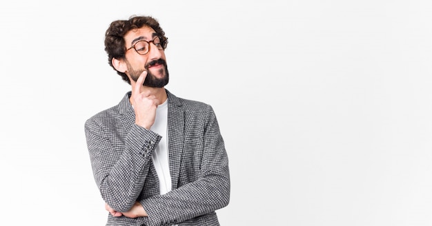 Young crazy businessman smiling happily and daydreaming or doubting, looking to the side on flat wall