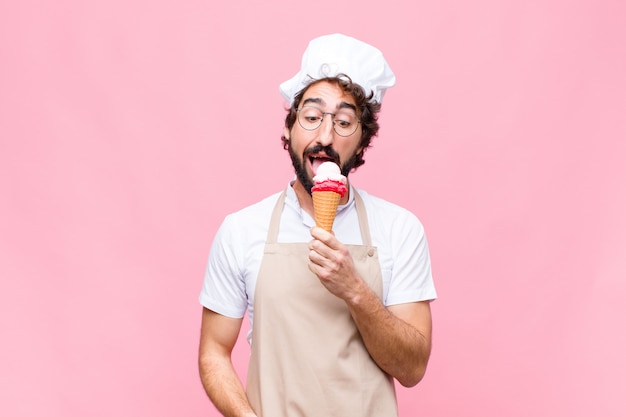 Young crazy chef man with an ice cream against pink wall