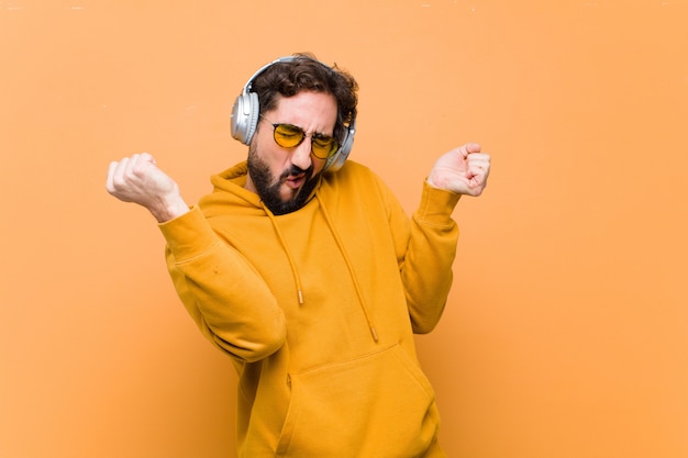 Young crazy cool man listening music with headphones against orange wall