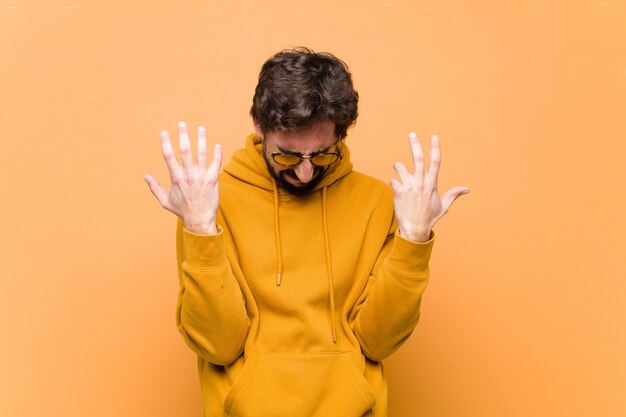 Young crazy cool man sad expression against orange wall