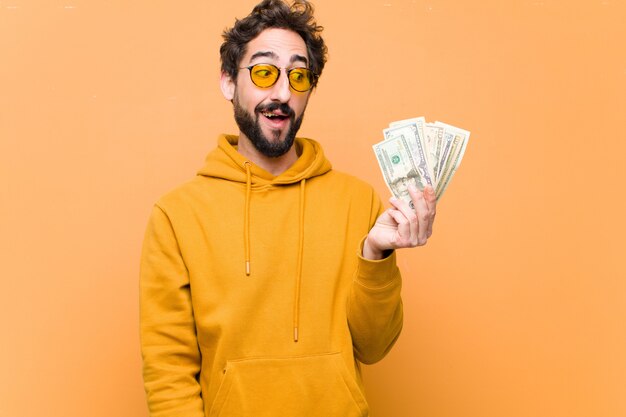 Photo young crazy cool man with dollar banknotes against orange wall