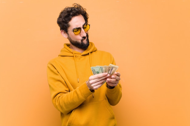 Young crazy cool man with dollar banknotes on orange wall