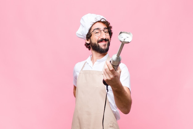 Young crazy cool man with a hand blender over pink wall