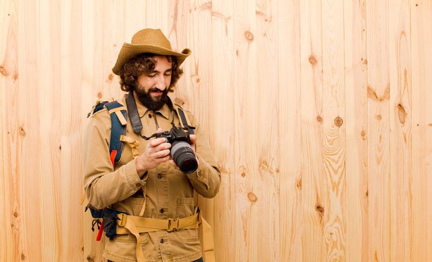 Young crazy explorer with straw hat and backpack on wooden wall 