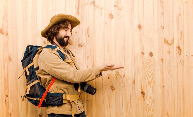 Young crazy explorer with straw hat and backpack on wooden wall 