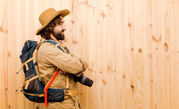 Young crazy explorer with straw hat and backpack on wooden wall 