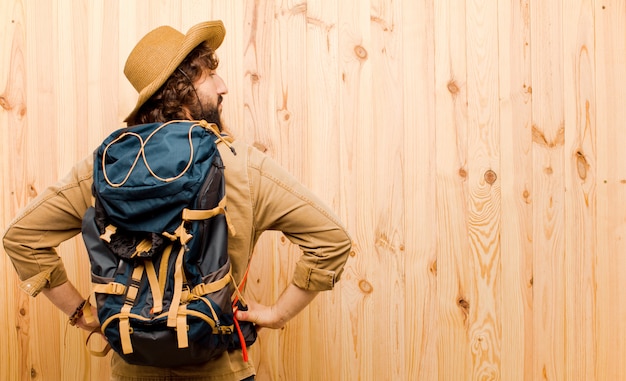 Young crazy explorer with straw hat and backpack on wooden wall