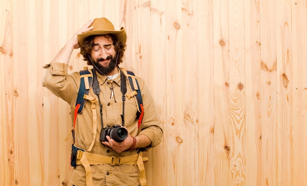 Young crazy explorer with straw hat and backpack on wooden wall