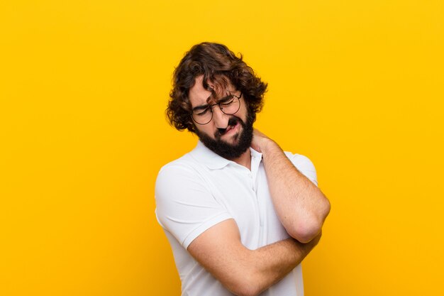 Young crazy man feeling anxious, ill, sick and unhappy, suffering a painful stomach ache or flu against yellow wall