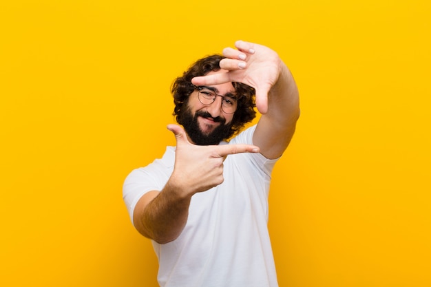 Young crazy man feeling happy, friendly and positive, smiling and making a portrait or photo frame with hands