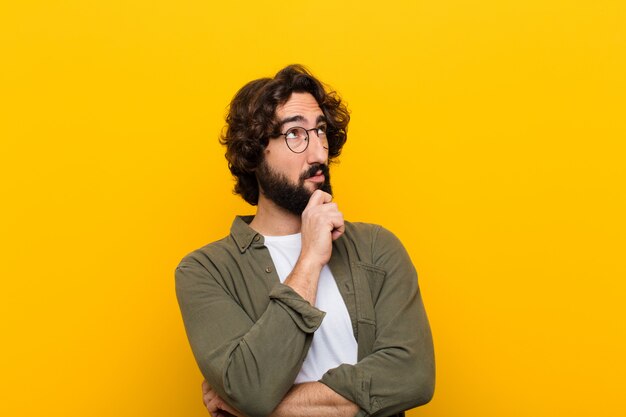 Photo young crazy man feeling thoughtful, wondering or imagining ideas, daydreaming and looking up to copyspace against yellow wall