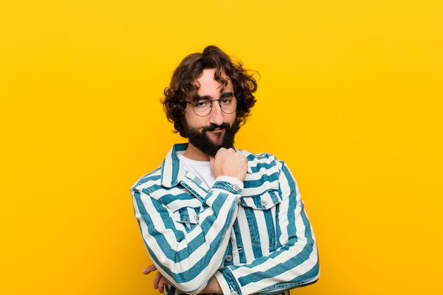 Young crazy man looking serious, confused, uncertain and thoughtful, doubting among options or choices against yellow wall