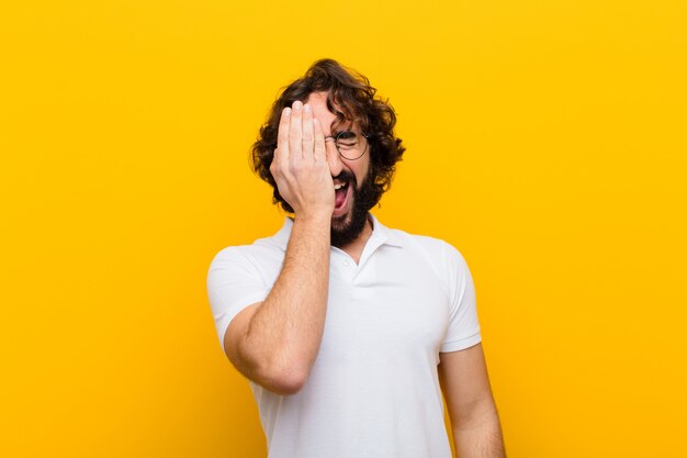 Young crazy man looking sleepy, bored and yawning, with a headache and one hand covering half the face