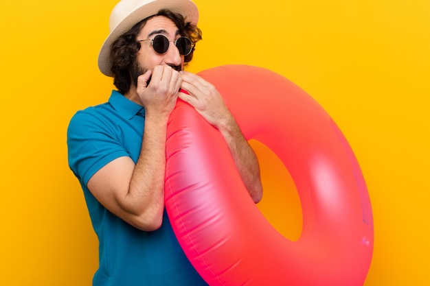 Young crazy man looking worried, anxious, stressed and afraid, biting fingernails and looking to lateral copyspace  orange wall