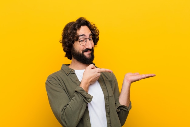 Young crazy man smiling cheerfully and pointing to copy space on palm on the side showing or advertising an object