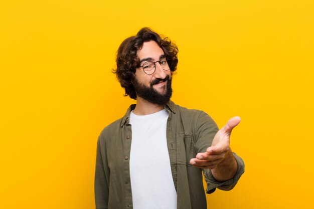 Young crazy man smiling, looking happy, confident and friendly, offering a handshake to close a deal, cooperating