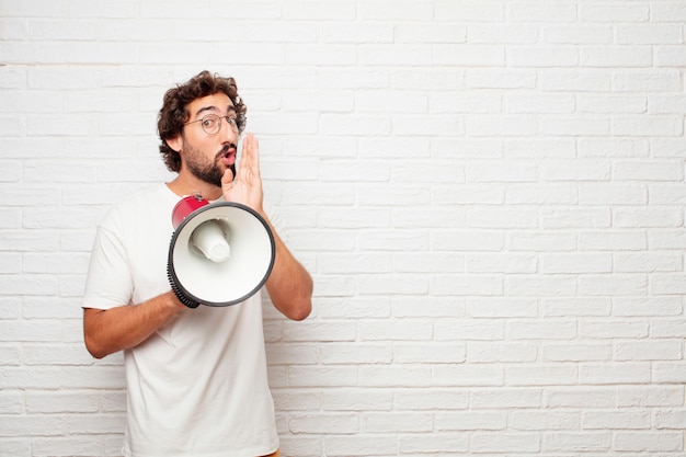 Young crazy man with a megaphone against brick wall.