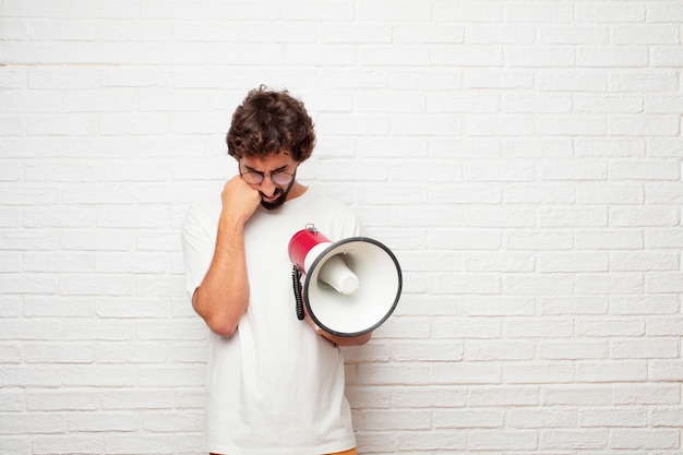 Young crazy man with a megaphone against brick wall.