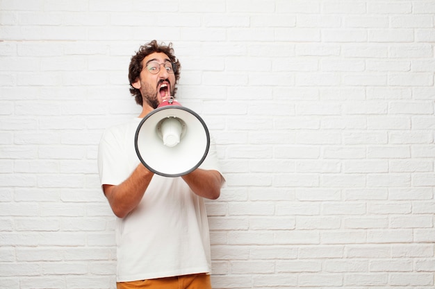 Young crazy man with a megaphone against brick wall.