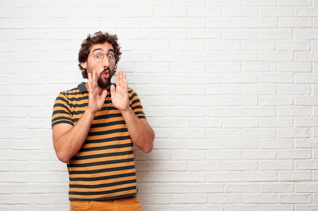 Young crazy or silly man gesturing and expressing emotions against brick wall background