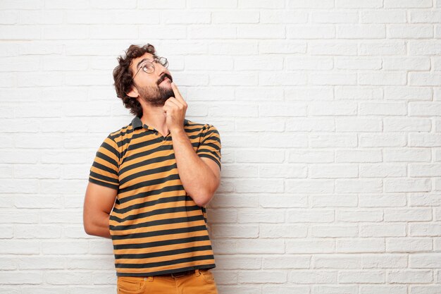 Young crazy or silly man gesturing and expressing emotions against brick wall background