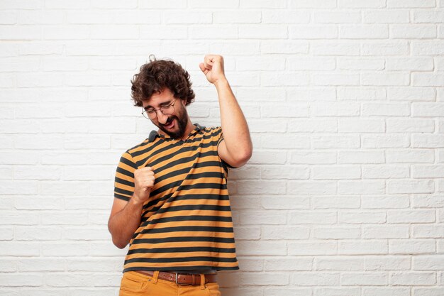 Young crazy or silly man gesturing and expressing emotions against brick wall background