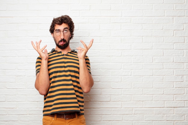 Young crazy or silly man gesturing and expressing emotions against brick wall background