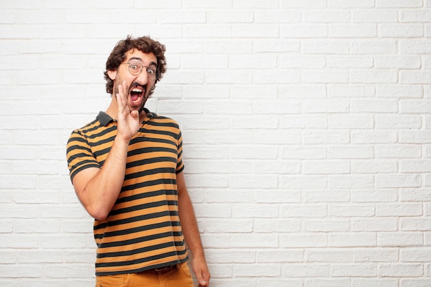 Giovane pazzo o uomo sciocco che gesturing e che esprime le emozioni contro il fondo del muro di mattoni