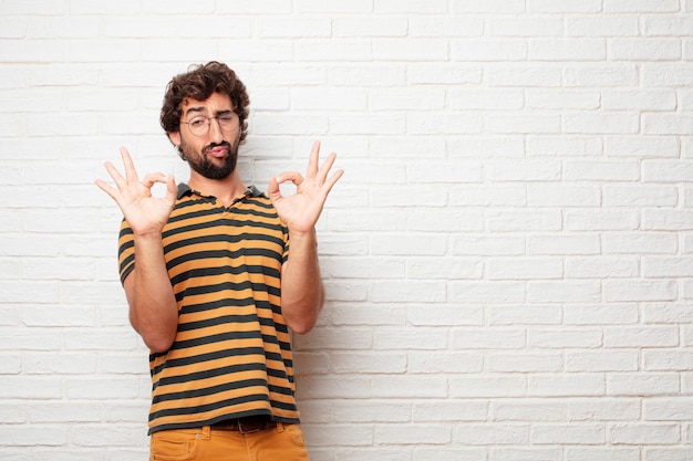 Young crazy or silly man gesturing and expressing emotions against brick wall background