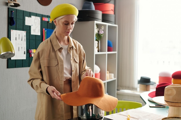Young creative craftswoman steaming new hat over pan with boiling water