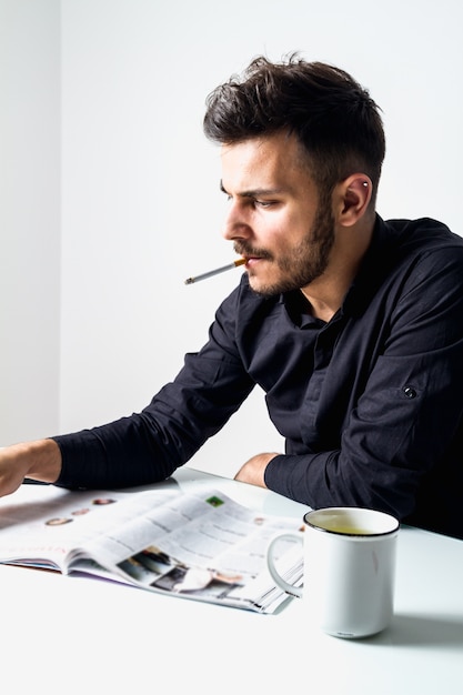 若いクリエイティブディレクター喫煙タバコと彼のオフィスで雑誌を読む