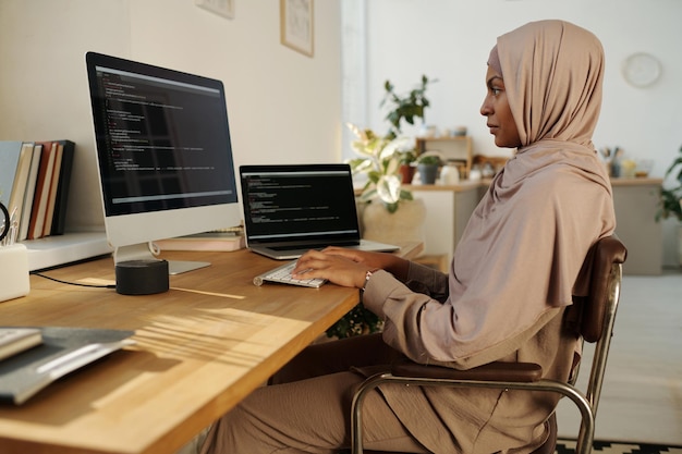 Young creative female webdesigner typing on computer keyboard and looking at screen