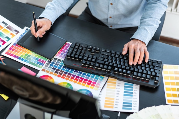 Young creative graphic designer working on color selection and drawing on graphics tablet at workplace Color swatch samples chart for selection coloring