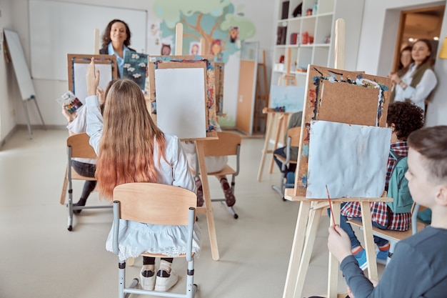 Foto i giovani alunni felici creativi in aula moderna leggera stanno facendo lezione di disegno