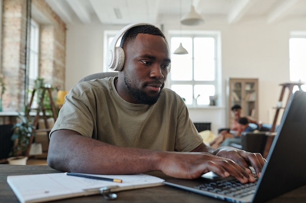 Young creative male designer in headphones pressing laptop buttons while working over new online project or presentation in home environment