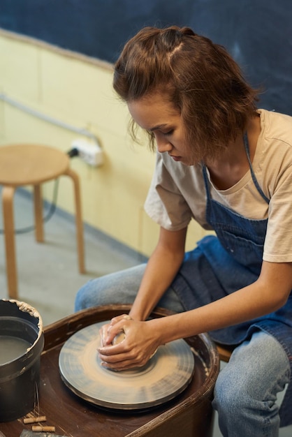 Young creative woman sitting by rotating pottery wheel