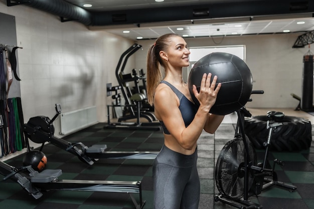 Young cross fit woman exercising with medicine ball in the modern gym. Functional training. Healthy lifestyle