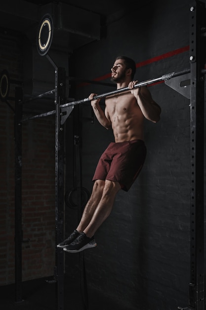 Young crossfit athlete doing pullups at the gym. Strong man doing functional training