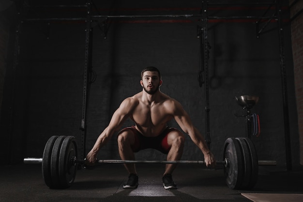 Young crossfit athlete lifting barbell at gym. Muscular shirtless man