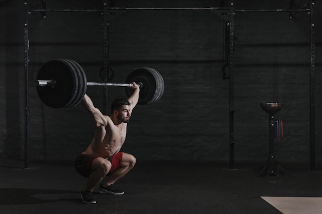 Giovane atleta crossfit che solleva il bilanciere in testa in palestra spazio di copia