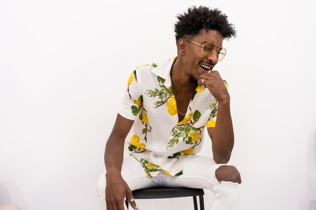 A young Cuban seated in a white flowered shirt and glasses. Smiling and dancing on a white background